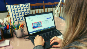 zdjęcie przedstawia laptopa z otwartą stroną PRzejścia Dialogu. Laptop obsługuje osoba z blond włosami, sfotografowana z wysokości jej lewego ramienia.