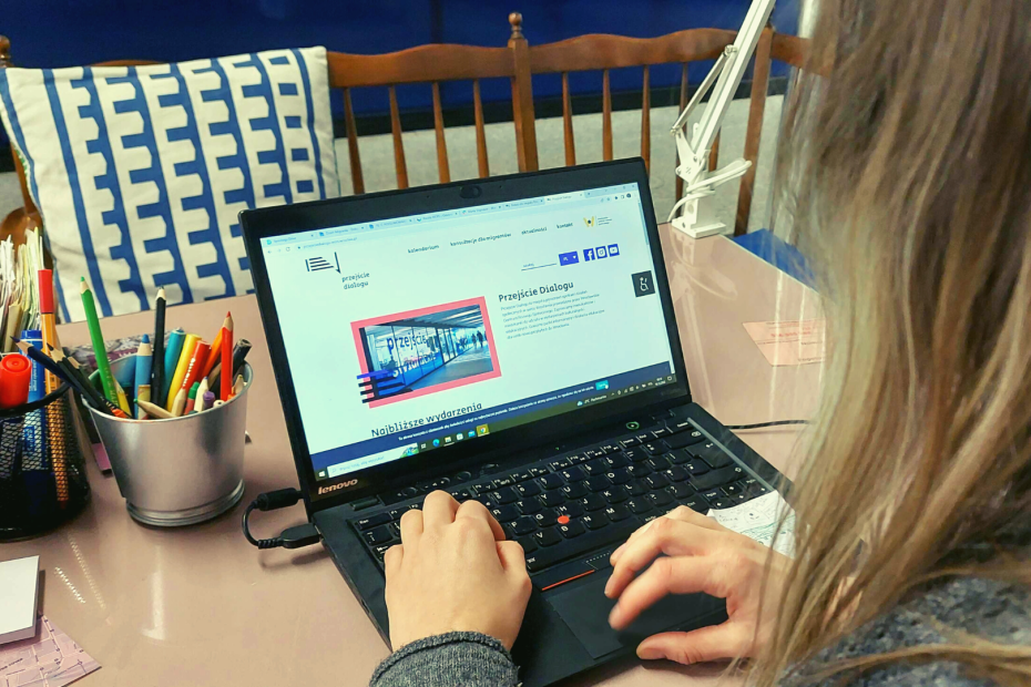 zdjęcie przedstawia laptopa z otwartą stroną PRzejścia Dialogu. Laptop obsługuje osoba z blond włosami, sfotografowana z wysokości jej lewego ramienia.